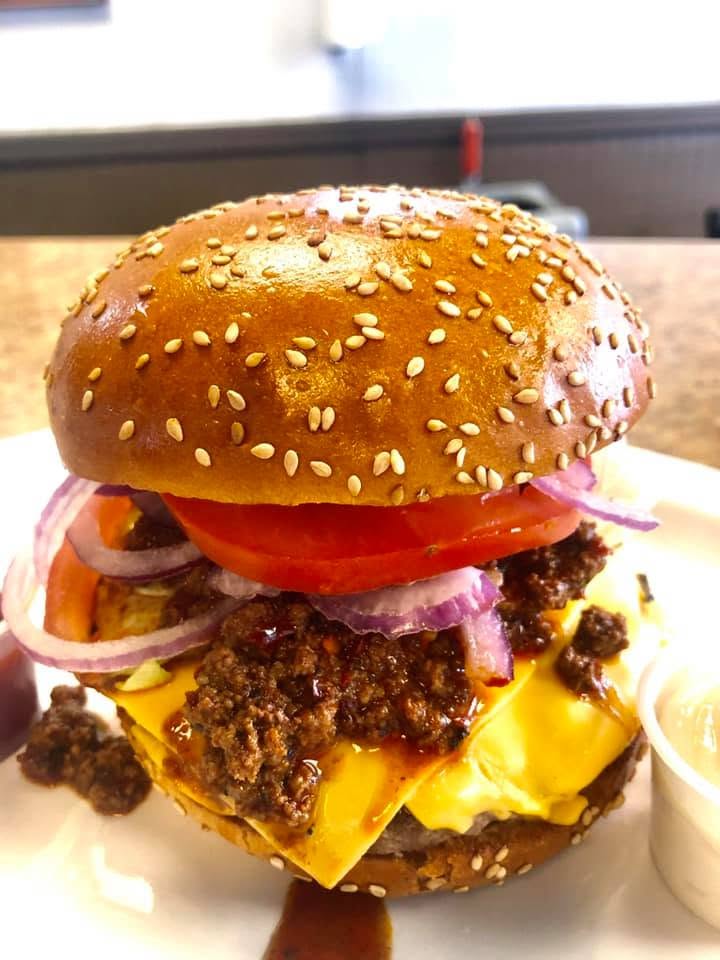 Hamburger topped with chili, cheese, tomato and red onion on a sesame bun