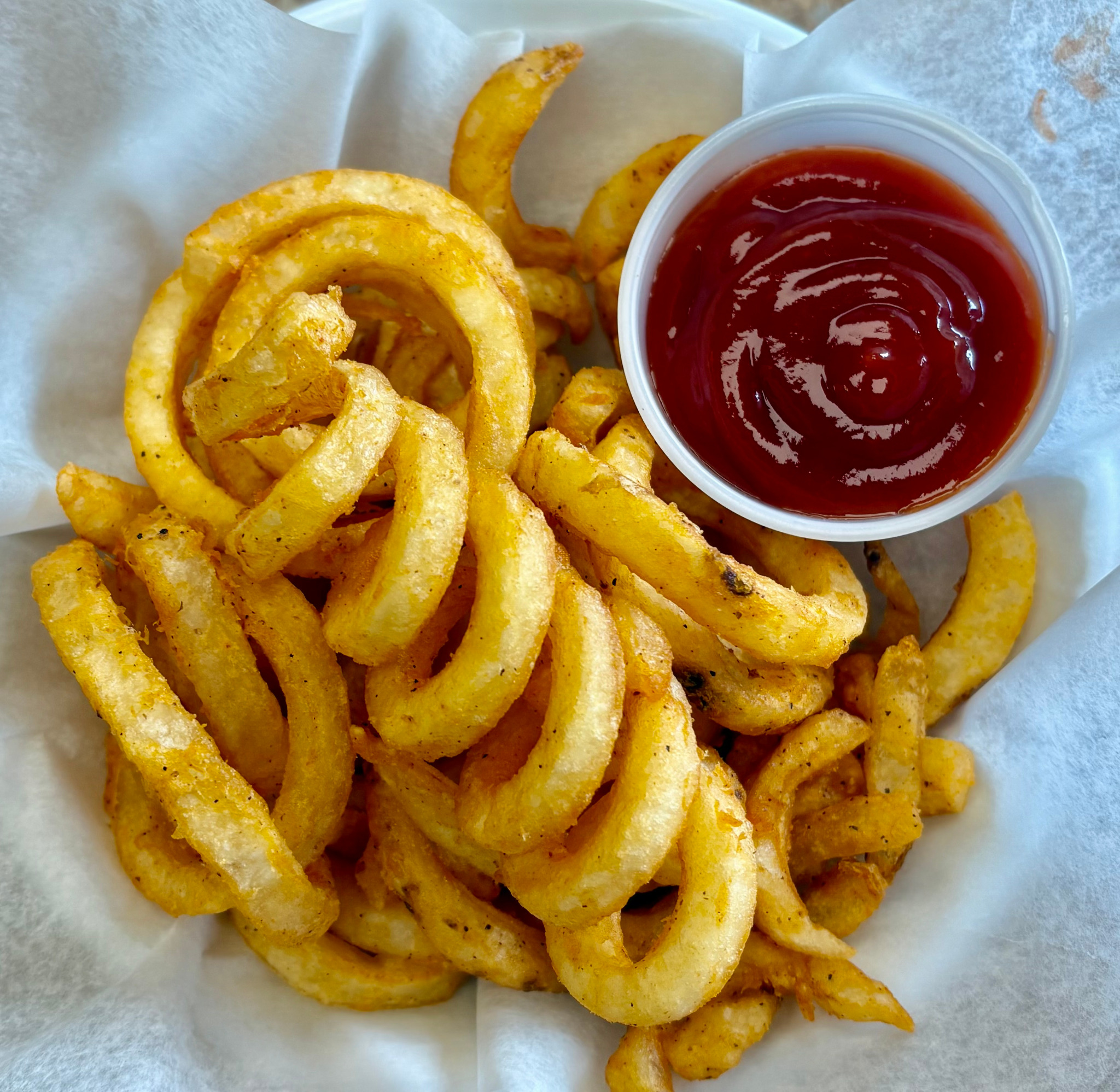 Golden curly fries with a cup of ketchup