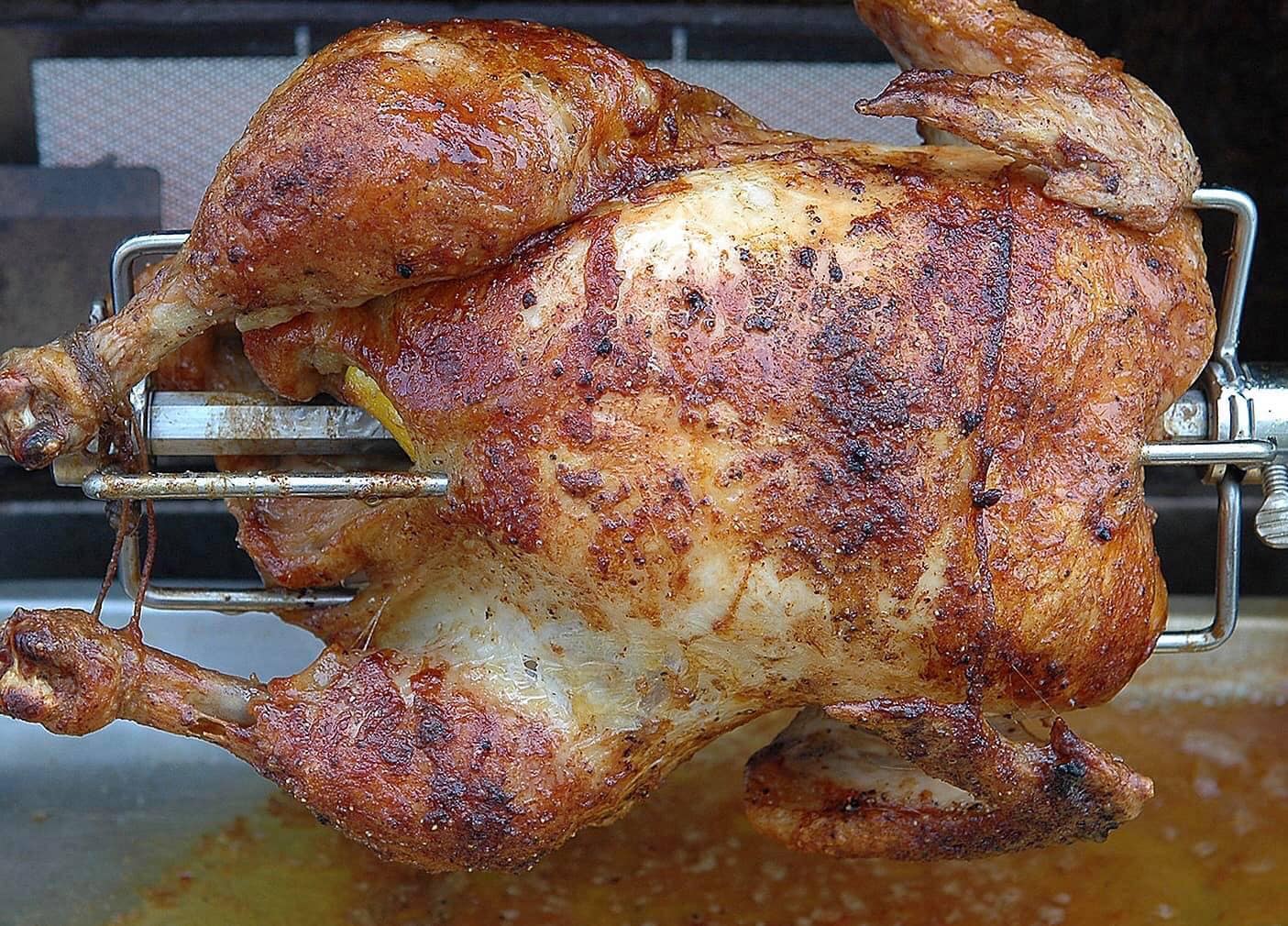 Golden-brown whole chicken on a rotisserie spit, fresh from the oven